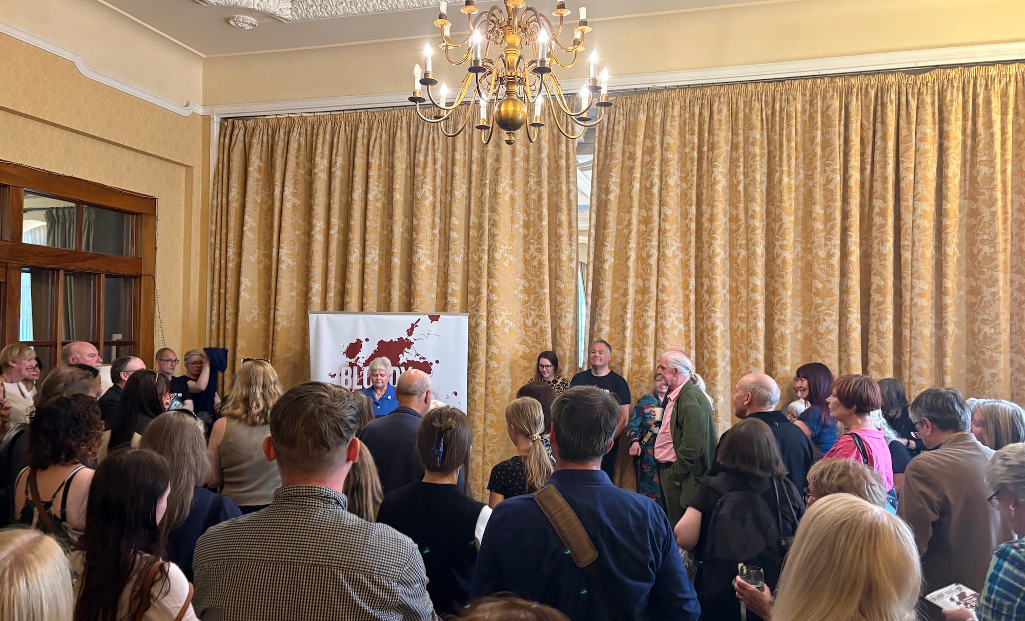 A group of people in a large hotel conference room, in front of a Bloody Scotland banner