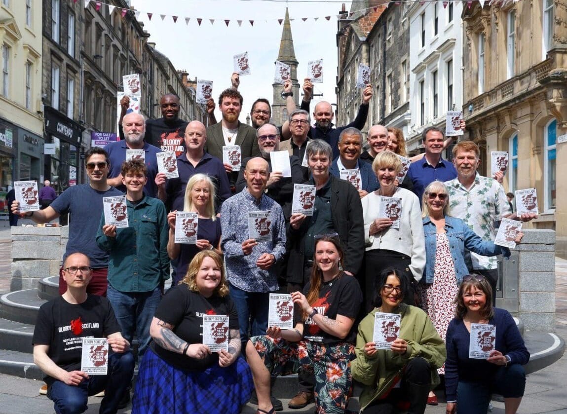 A large group of authors on Stirling high street, holding the programme for Bloody Scotland