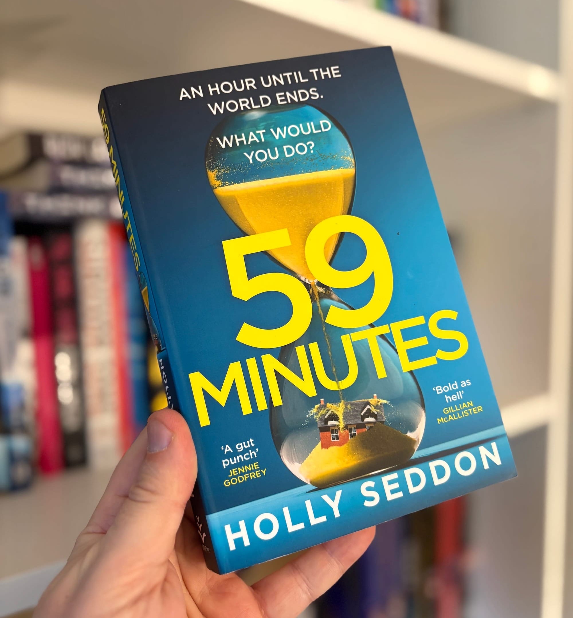 The cover of 59 Minutes by Holly Seddon, featuring a large hourglass with sand flowing over a house