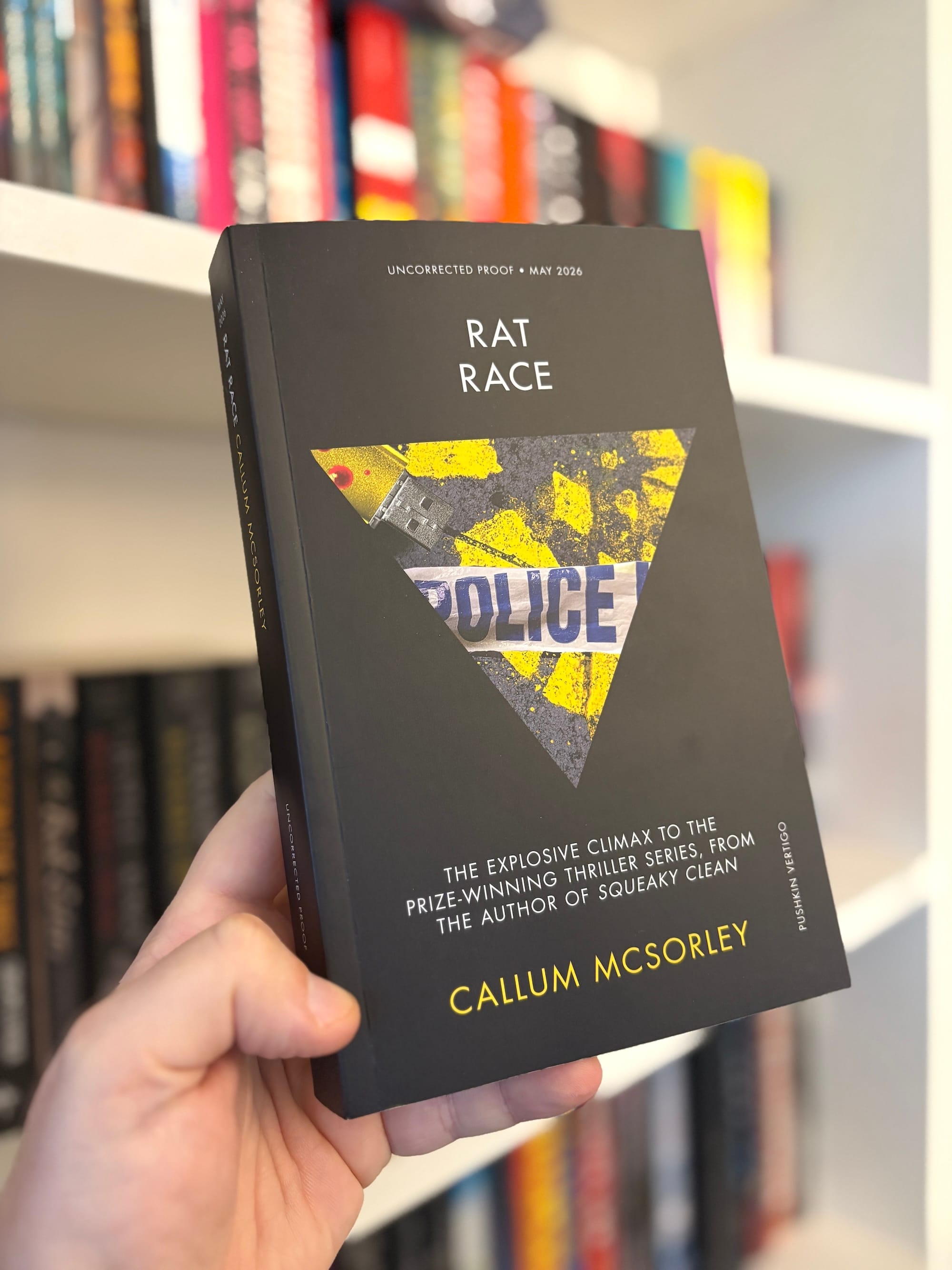 A proof copy of RAT RACE by Callum McSorley, featuring a black cover with police tape over a yellow footprint