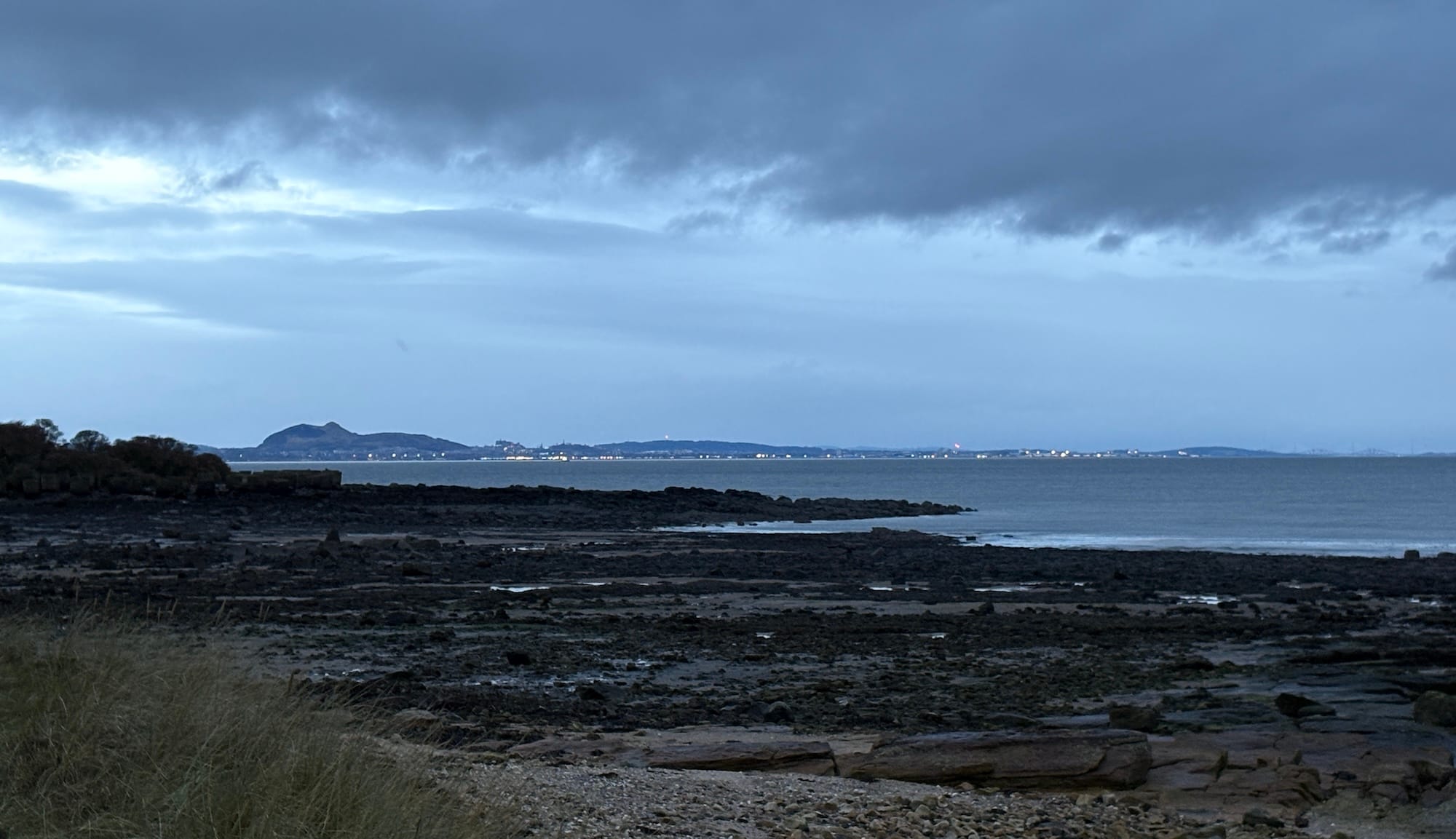 A rocky foreshore, grey skies and Edinburgh in the distance