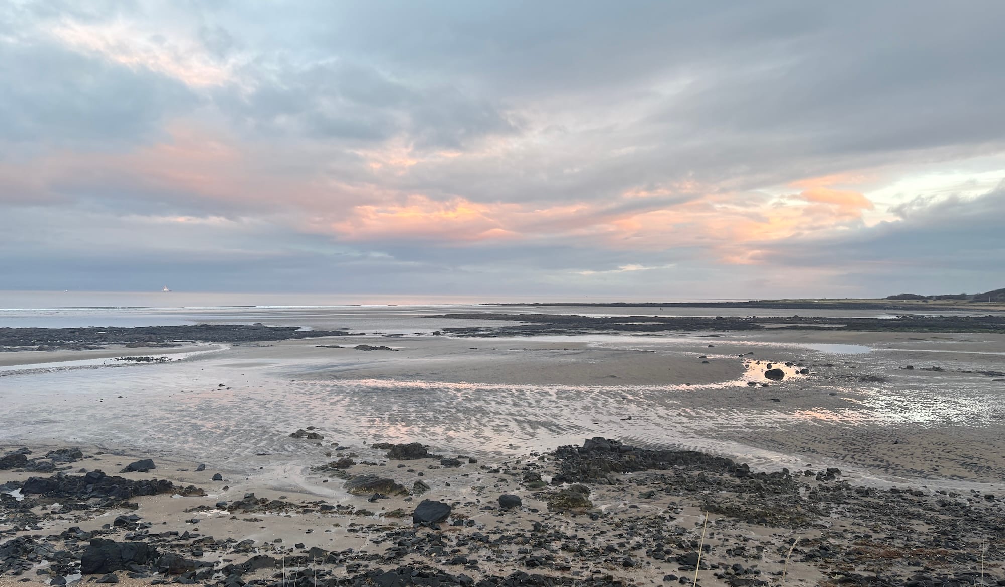 A sandy and rocky beach with sunlit clouds overhead